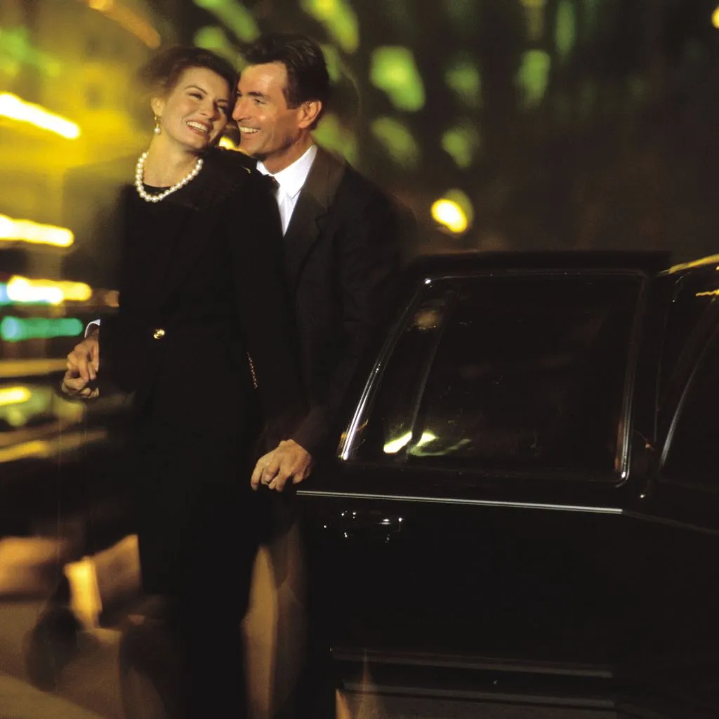 Elegant couple enjoying a romantic evening, standing by a black luxury sedan after using the premium Night Out Limo Service in Muskoka.